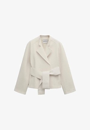 Crèmekleurig damesblazer met brede revers, lange mouwen en een bijpassende stoffen riem gestrikt in de taille, plat gelegd op een witte achtergrond.