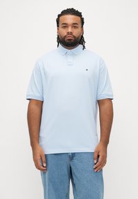 Lyseblå polo med krave, korte ærmer og et lille logo på brystet. Parret med falmede blå denimjeans.