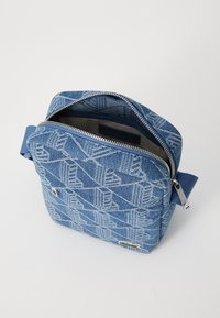 Kék farmer keresztpántos táska geometrikus mintával, tetején cipzáros záródással, textil pánttal, és egy kis logóval. Belseje bélelt és semleges színű.