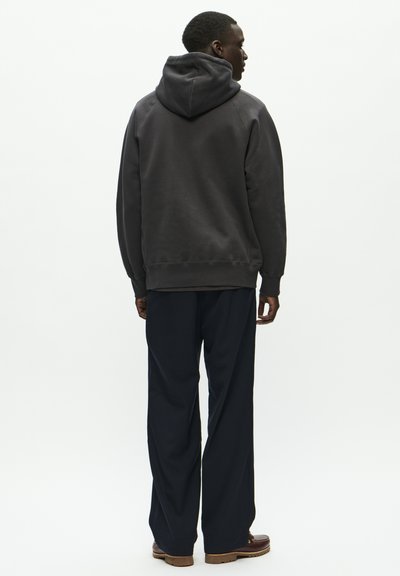 Siva kapuca, mehak tekstur, sproščen kroj, z ribanim zaključkom rokavov. V kombinaciji s temno mornarsko širokimi hlačami in rjavimi čevlji.