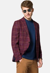 Bordo kraciasty żakiet z niebieskimi akcentami, z pojedynczym zapięciem na guzik, z wyciętymi klapami, noszony na niebieskiej koszuli, w zestawie z brązowymi spodniami.