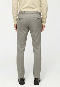 Grijze wollen broek met een gestructureerd patroon, slim fit, twee achterzakken met ritsen en een gladde tailleband. G gedragen met zwarte schoenen.