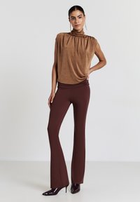 Haut marron à manches courtes avec encolure froncée, associé à un pantalon bordeaux ajusté et évasé. Texture lisse ; modèle portant des talons à bout pointu.