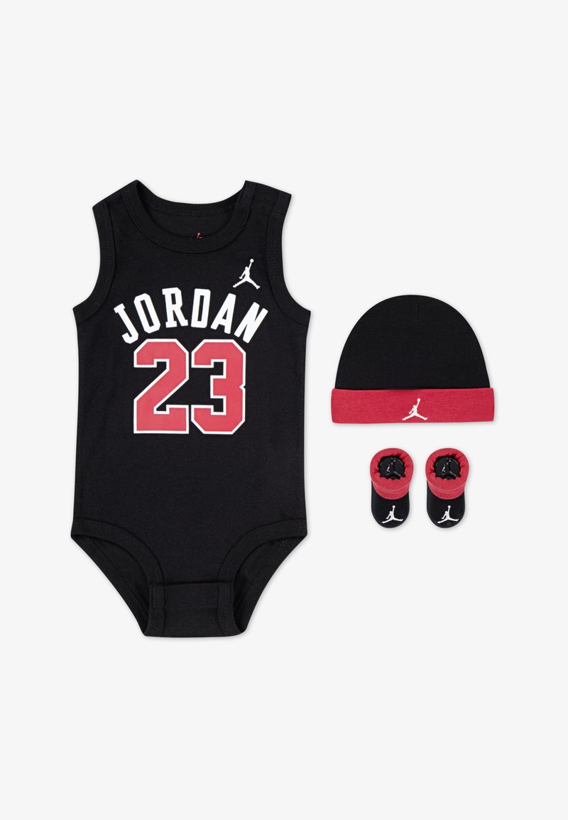 Une combinaison en coton noir avec "JORDAN" et "23" en blanc et rouge. Comprend un bonnet noir avec un bandeau rouge et des chaussons assortis avec le logo.