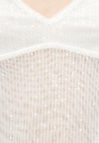 Λευκό δίχτυ με κάθετες σειρές από μικρές παγιέτες πάνω σε δέρμα, με λαιμόκοψη σε σχήμα V.