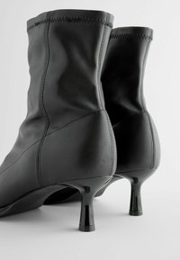 Black leather ankle boots with a smooth texture, curved design, and glossy stiletto heels. Features visible stitching and a streamlined silhouette.