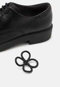 Schwarzer Lederschuh mit abgerundetem Zeh, einfarbigen Schnürsenkeln und strukturiertem Sohlen, kombiniert mit einem schwarzen, gummiartigen, blütenförmigen Zubehör.