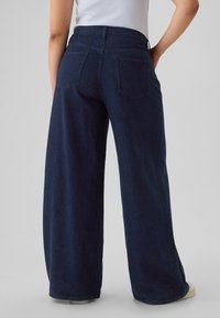 Sötétkék széles szárú farmernadrág sima textúrával, ötpocketes kialakítással és magas derékrésszel. Finom varrási részletekkel elérhető.