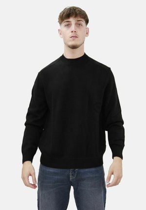 Maglione nero in maglia con collo rotondo e polsini a coste, abbinato a jeans blu. Design semplice, senza motivi o loghi visibili.