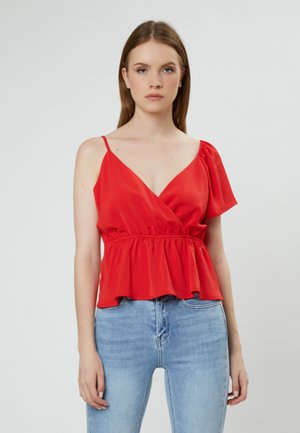 Top peplum de seda roja con un profundo escote en V, una sola manga con volantes y una cinturilla elástica. Llevado con jeans de tiro alto de color azul claro.