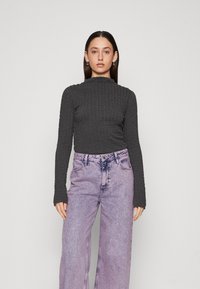 Mørk grå topp med lange ermer og strukturert overflate, høy hals, kombinert med høyt liv, vide lyse lilla jeans med en falmet vask.