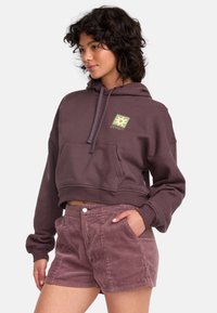 Cropped, dark purple hoodie with a front pocket and logo, paired with light purple corduroy shorts featuring side pockets and button closure.