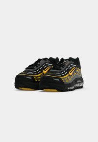 Een paar zwart-gouden Nike sneakers met reflecterende strepen en zichtbare luchtkussens in de zool, getoond vanuit een driekwart frontale hoek.