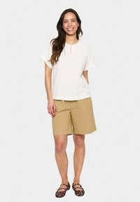 Svetlobežový textúrovaný top s okrúhlym výstrihom a krátkymi rukávmi v kombinácii s khaki šortkami. Outfit dopĺňajú čierne a hnedé vzorované baleríny.