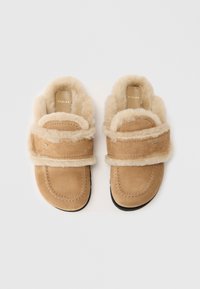 Pantofole in suede beige con un morbido rivestimento in pelliccia sintetica e cinturino. Forma della punta arrotondata, dettagli cuciti e suola in gomma nera.