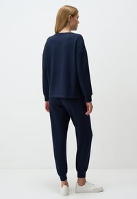 Felpa navy e pantaloni jogger abbinati in tessuto morbido; vestibilità rilassata con orli elasticizzati; abbinati a sneakers bianche. Nessun motivo o accento visibile.