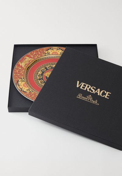 Κεραμικό πιάτο με περίπλοκα χρυσά και κόκκινα σχέδια, τοποθετημένο σε μαύρο κουτί με χρυσή επιγραφή «Versace» και το λογότυπο «Rosenthal».