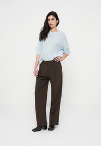 Ανοιχτό μπλε πλεκτό πουλόβερ με κοντά μανίκια, συνδυασμένο με καφέ παντελόνι ψηλόμεσο και φαρδιά μπατζάκια και γυαλιστερά μαύρα παπούτσια.