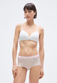 Balta paminkštinta liemenėlė su plonomis petnešėlėmis, derinama su šortais su gėlių raštu ir šviesiai rožinės spalvos elastingu juosmeniu, pažymėtu užrašu „PIECES.“