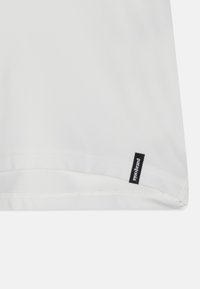 Bílý bavlněný tričko s hladkým povrchem. Obsahuje černou etiketu s logem Patagonia blízko spodního lemu. Jednoduchý a minimalistický design.