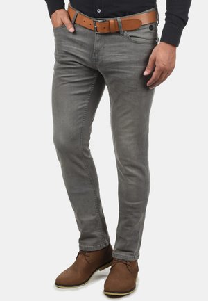 Jeans slim-fit grises con una textura suave, que cuentan con cinco bolsillos, un cinturón de cuero marrón y botas de tobillo marrones.