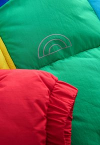 Kolorowe poduszki pikowane w czerwonym, zielonym, żółtym i niebieskim. Oferują gładką fakturę z haftowanym wzorem tęczy na zielonym materiale.
