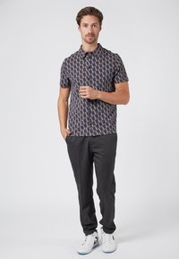 Camisa de manga corta con un patrón geométrico azul y marrón, combinada con pantalones oscuros grises y zapatillas blancas. Textura de tela suave.