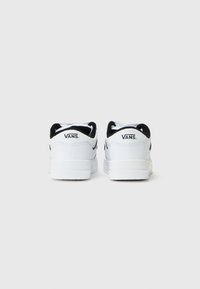 Baskets Vans blanches avec des accents noirs, en cuir lisse, avec un col rembourré et un logo bien visible sur le talon. Semelle en caoutchouc plate.