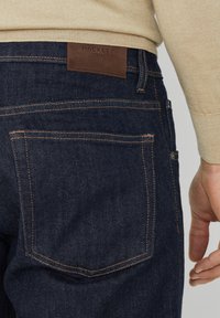 Granatowe dżinsy wykonane z denimu, z brązową skórzaną metką Hackett na pasku, pomarańczowymi szwami oraz dwoma tylnymi kieszeniami bez ozdób.