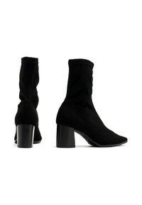 Czarne botki za kostkę wykonane z miękkiego materiału, z dopasowanym krojem, słupkowym obcasem, spiczastym noskiem i unikalnym detalem w postaci przeszyć.