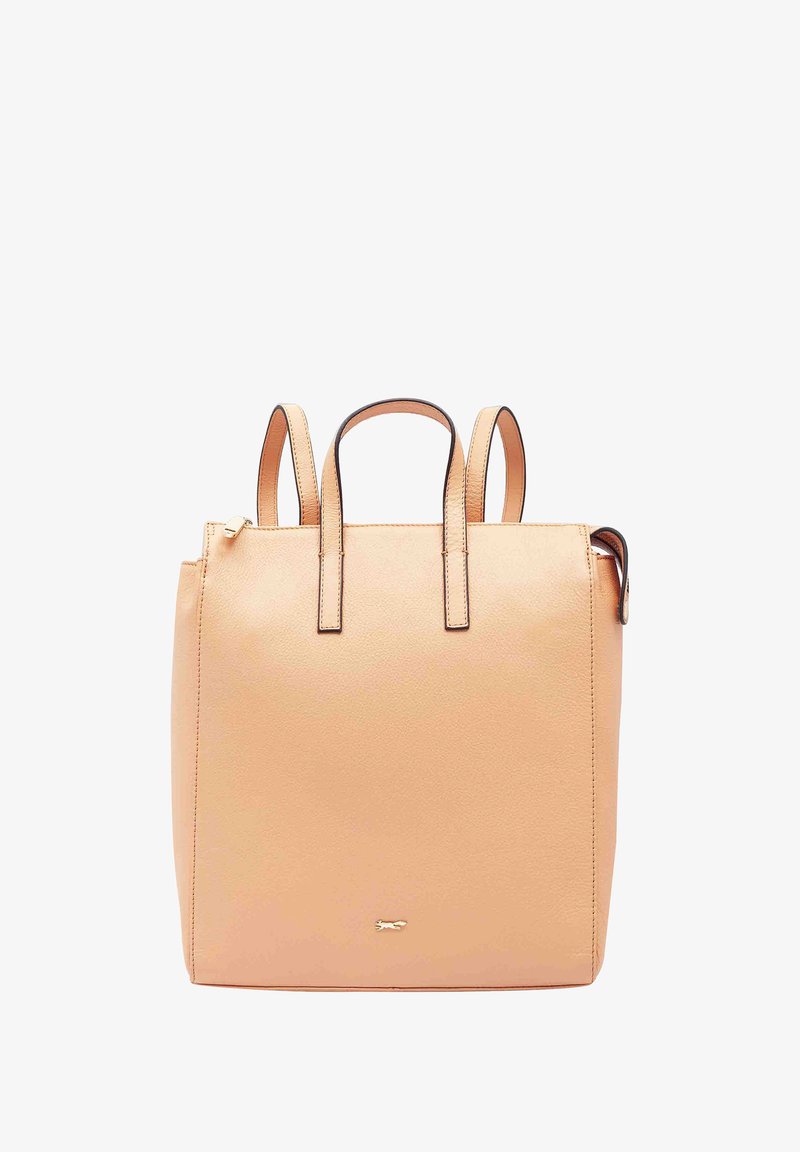 Sac à dos en cuir couleur pêche avec doubles poignées supérieures, design minimaliste et accent logo doré à l'avant. Fermeture éclair sur le côté.