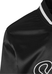 Veste en satin noir avec un col rayé blanc et un logo brodé en relief sur la poitrine, présentant une texture lisse et une coupe ajustée.