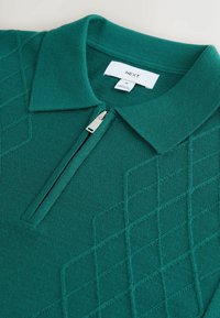Grünes Strick-Poloshirt mit hohem Kragen, halb kurzem Reißverschluss und strukturiertem Rautenmuster. Das Etikett zeigt "NEXT", Größe M. Weicher, mittelschwerer Stoff.
