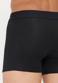 Schwarze Boxershorts aus glattem Stoff, mit einem breiten elastischen Bund und kontrastierenden Nähten entlang der Nähte für zusätzliche Details.