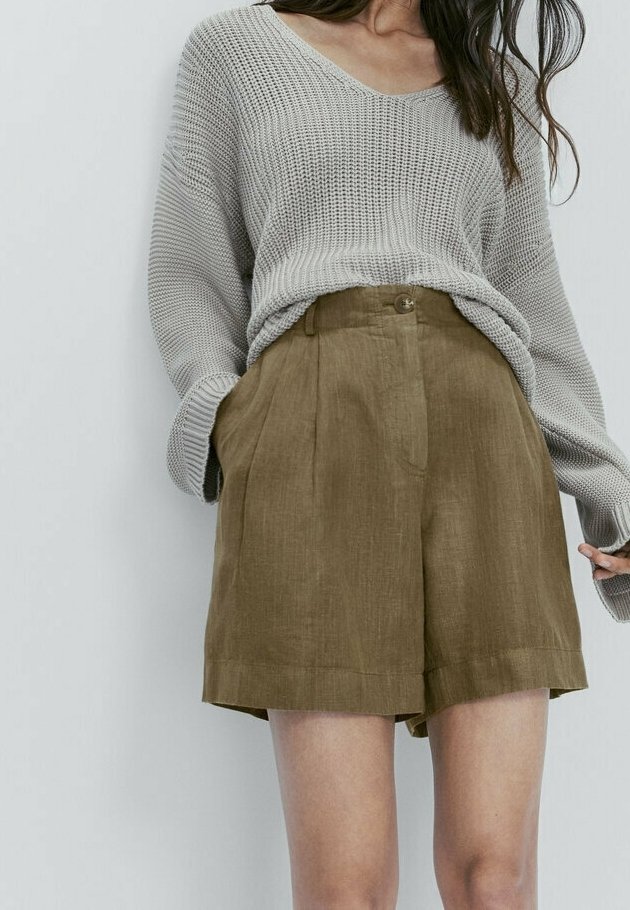 Pull en maille gris clair à col en V, associé à un short en lin brun taille haute avec des plis pressés et des poches latérales.