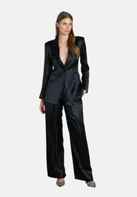 Zwart pinstripe pak van gladde stof; heeft een diep V-hals blazer met twee voorkambula en brede broekspijpen. Accenten van zilveren strepen.