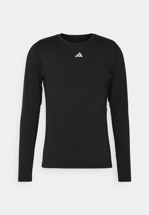 Chemise noire à manches longues avec un col rond, texture lisse et logo Adidas blanc sur la poitrine. Conception ajustée et construction sans coutures.