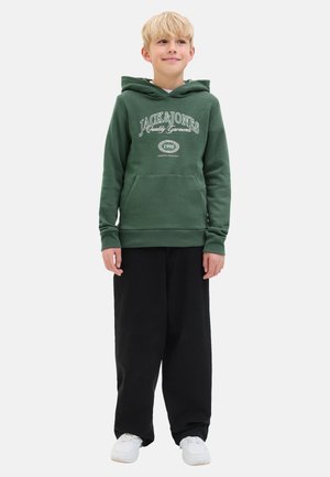 Grüne Kapuzenjacke mit einer Fronttasche und weißem aufgedrucktem Logo, kombiniert mit lockeren schwarzen Hosen und weißen Turnschuhen. Lässig, weicher Stoff.