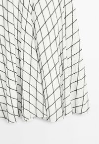 Hvidt stof med et sort diamantmønster, der har et let, tekstureret design. Kanterne er let buede. Ideel til lag-på-lag styling.
