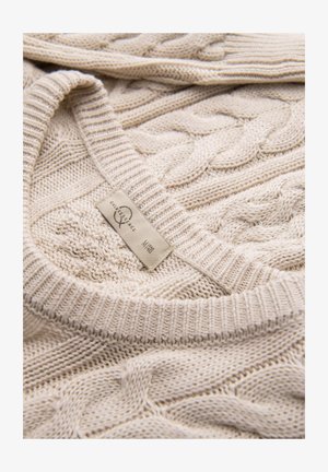 Pull en tricot beige avec un col côtelé et une texture. Étiquette visible indiquant la taille et la marque attachée au ourlet inférieur.