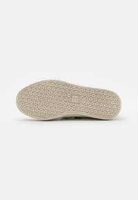 Light-colored sneaker sole with a hexagonal tread pattern and textured finish, featuring a logo in the center and a smooth edge.