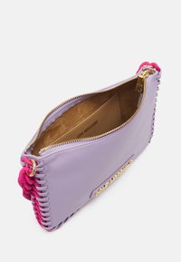 Fialová kožená kabelka s růžovými tkanými akcenty, zlatým kováním a zipovým uzávěrem. Interiér má béžovou podšívku s logem.