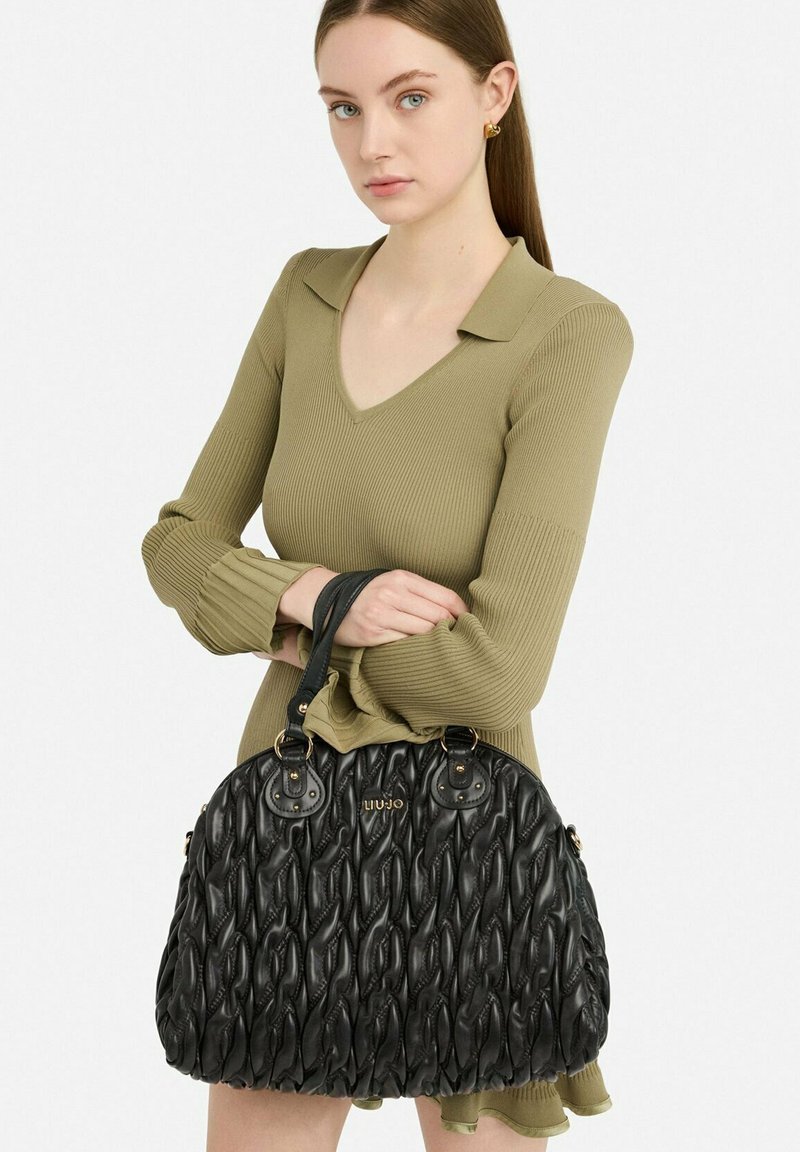 Zwarte leren handtas met gevlochten textuur en gouden hardware accenten. Voorzien van twee handgrepen en een afgeronde vorm. Het merklogo is duidelijk zichtbaar.