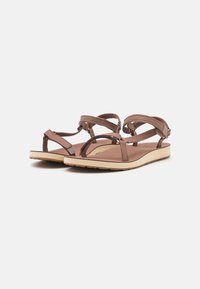 Brown leather sandals with crisscross straps, open toe design, flat sole, and beige rubber outsole. Lightweight and minimalistic style.