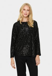 Top nero con paillettes, maniche lunghe e scollatura rotonda, caratterizzato da una vestibilità ampia e una superficie texturizzata e luccicante. Abbinato a pantaloni neri.