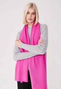 Sciarpa di lana di un brillante colore rosa, appoggiata su un maglione grigio, con una texture morbida e bordi rifiniti. La sciarpa è lunga, offrendo versatilità.