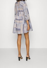 Blaue und beigefarbene gemusterte Kleid mit Dreiviertelärmel, plissiertem Rücken und ausgestelltem Rock, kombiniert mit schwarzen Absatzsandalen.