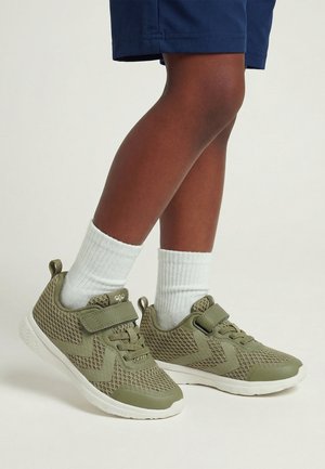 Dziecko noszące oliwkowo-zielone siateczkowe sneakersy z białymi podeszwami i paskami na rzepy, zestawione z białymi skarpetkami do kostki i granatowymi szortami.