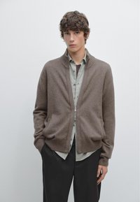 Brauner Reißverschluss-Cardigan mit geripptem Saum und Bündchen, aus weichem Material, getragen über einem hellgrünen Hemd mit Knöpfen und dunkler Hose.