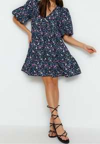Kwiatowa sukienka w granatowym kolorze z krótkimi bufiastymi rękawami, dekoltem w serek i rozkloszowanym dołem. Ozdobiona różowymi i białymi kwiatami. Zestawiona z czarnymi sandałami na paski.